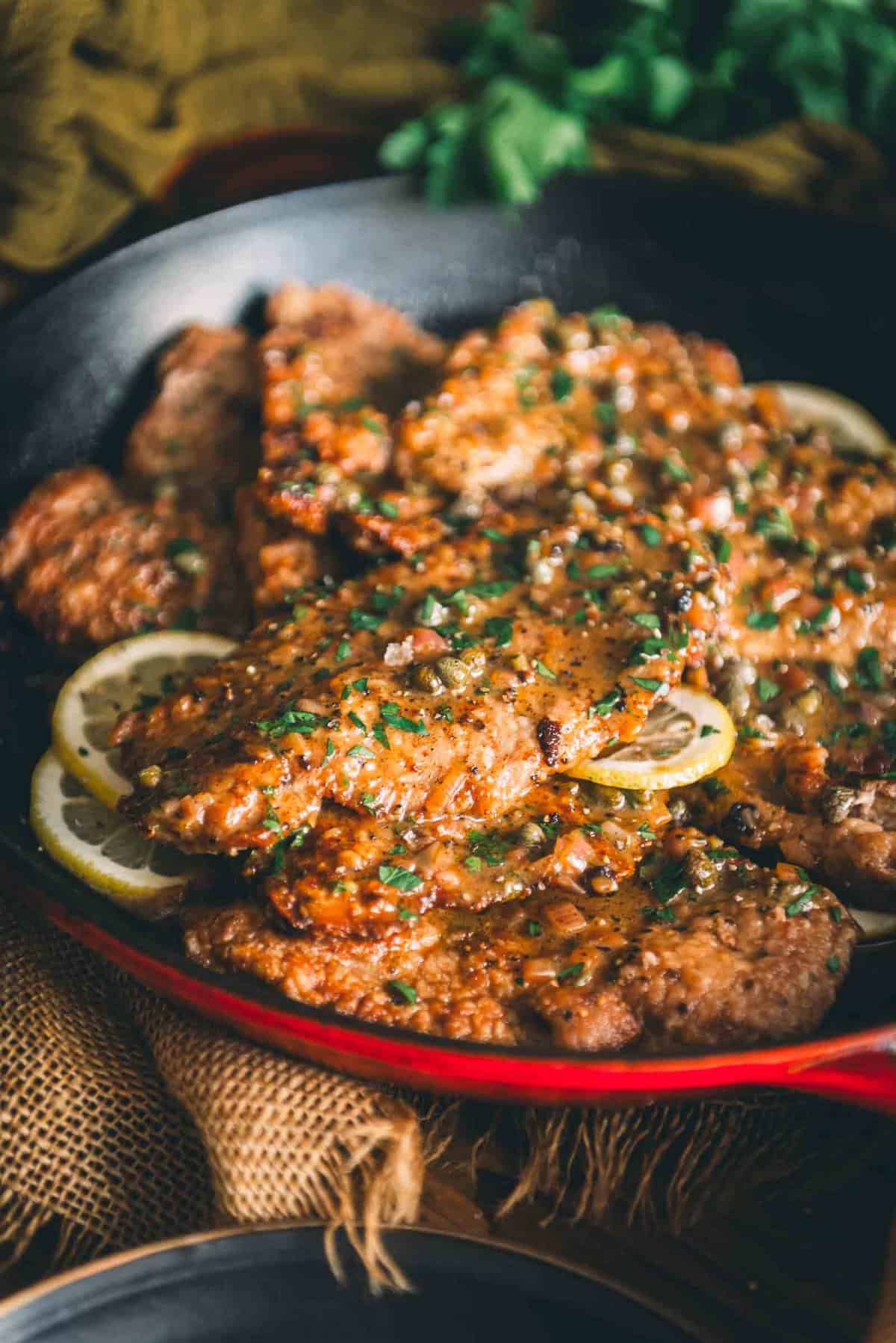 Veal cutlets in a skillet with lemon and parsley.