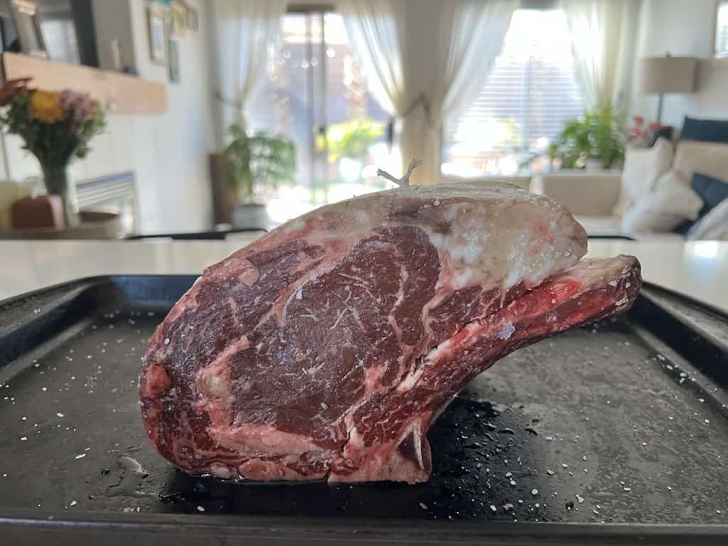 A mouthwatering prime rib roast sitting on a tray in a kitchen, after an overnight dry brine. 
