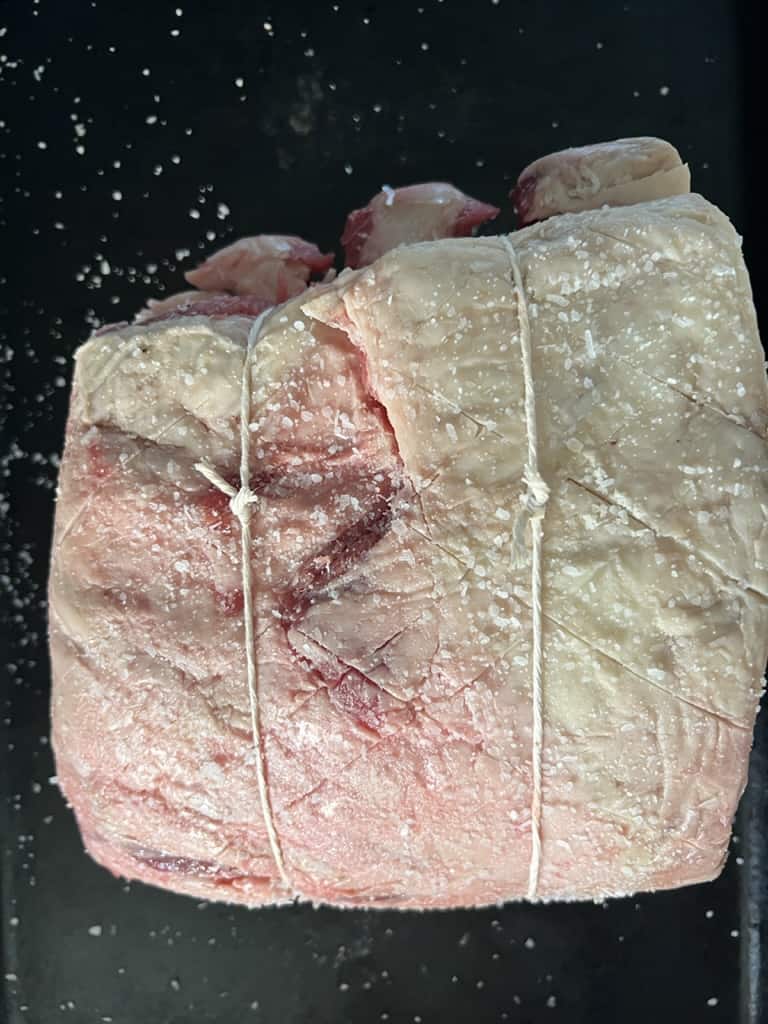 A rib roast, also known as a prime rib roast, is placed on a black tray.