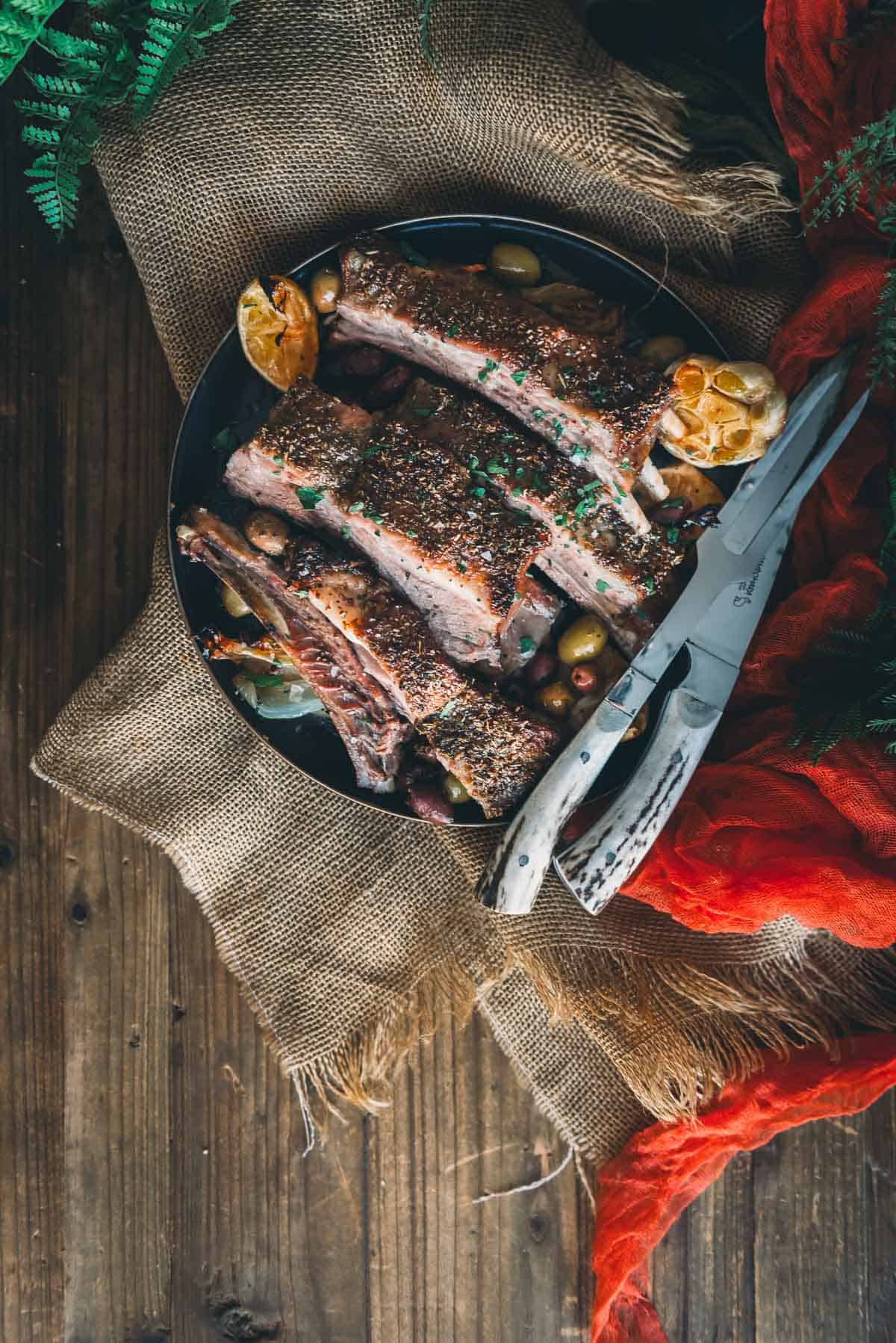 Lamb ribs on a black plate set onto a wooden table.