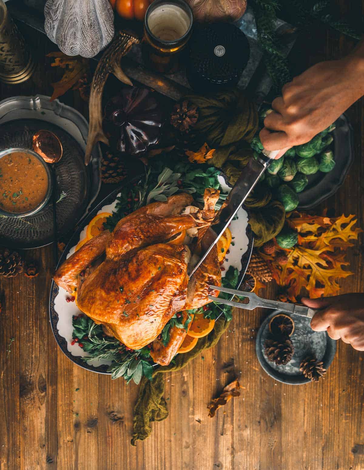 Hands holding fork and knife, carving into turkey. 