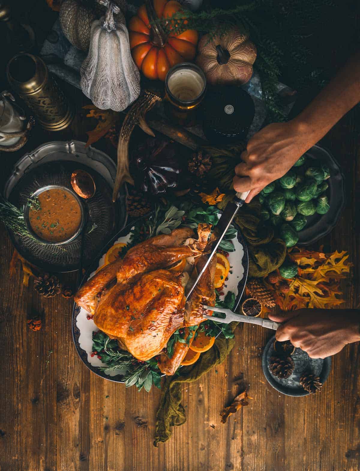 hands carving a turkey by removing the leg from the body with a chef's knife and fork. 