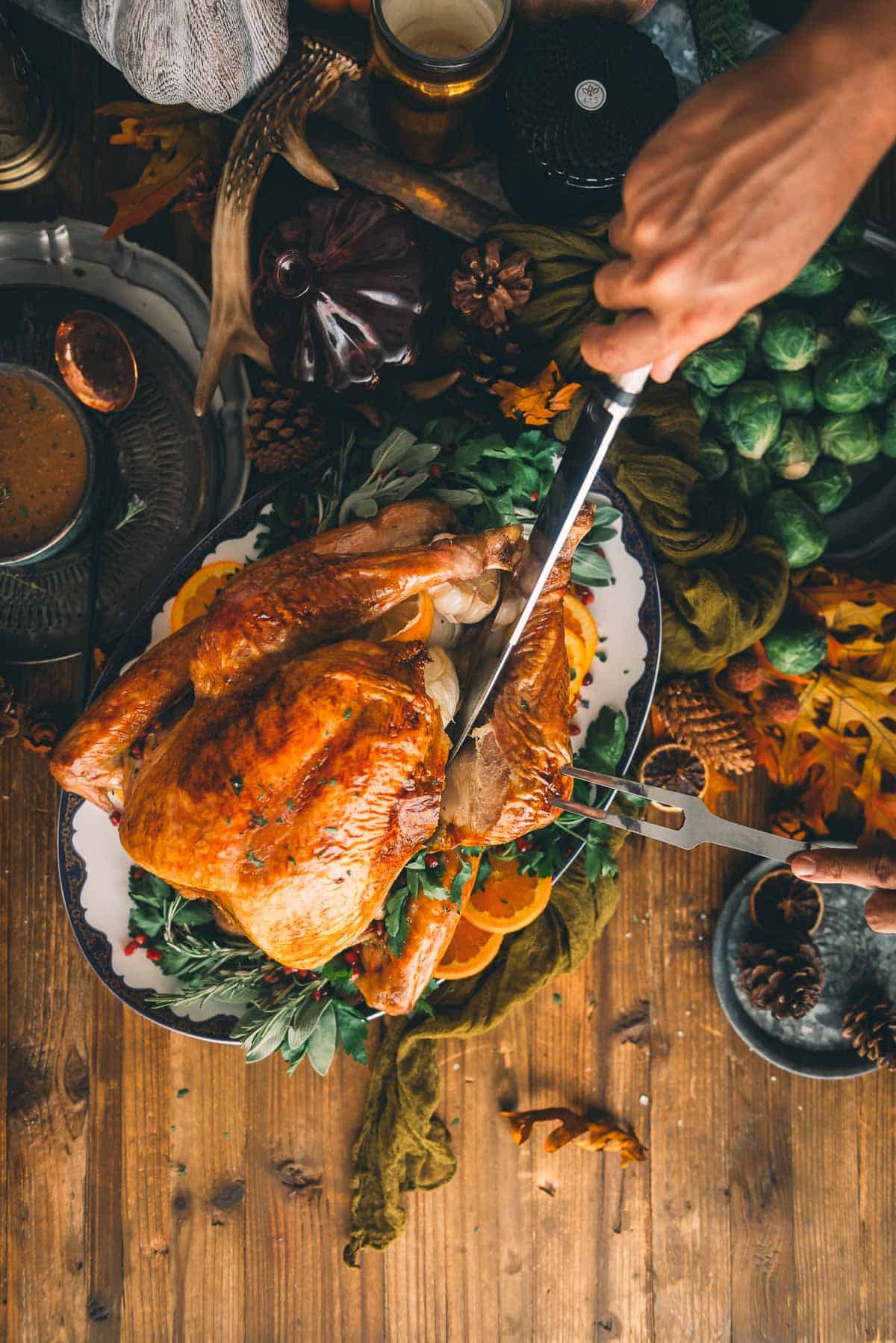 Hand holding fork and carving knife slicing into a turkey. 