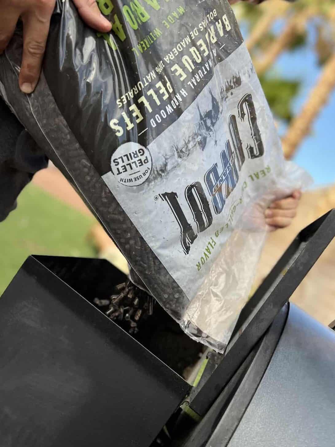 Bag of Cowboy brand charcoal pellets being poured into the hopper. 