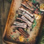 Tender lamb ribs sliced into individual ribs on a platter with olives, garlic and pomegranate seeds.