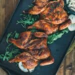 Smoked game hens on a black tray with greens.