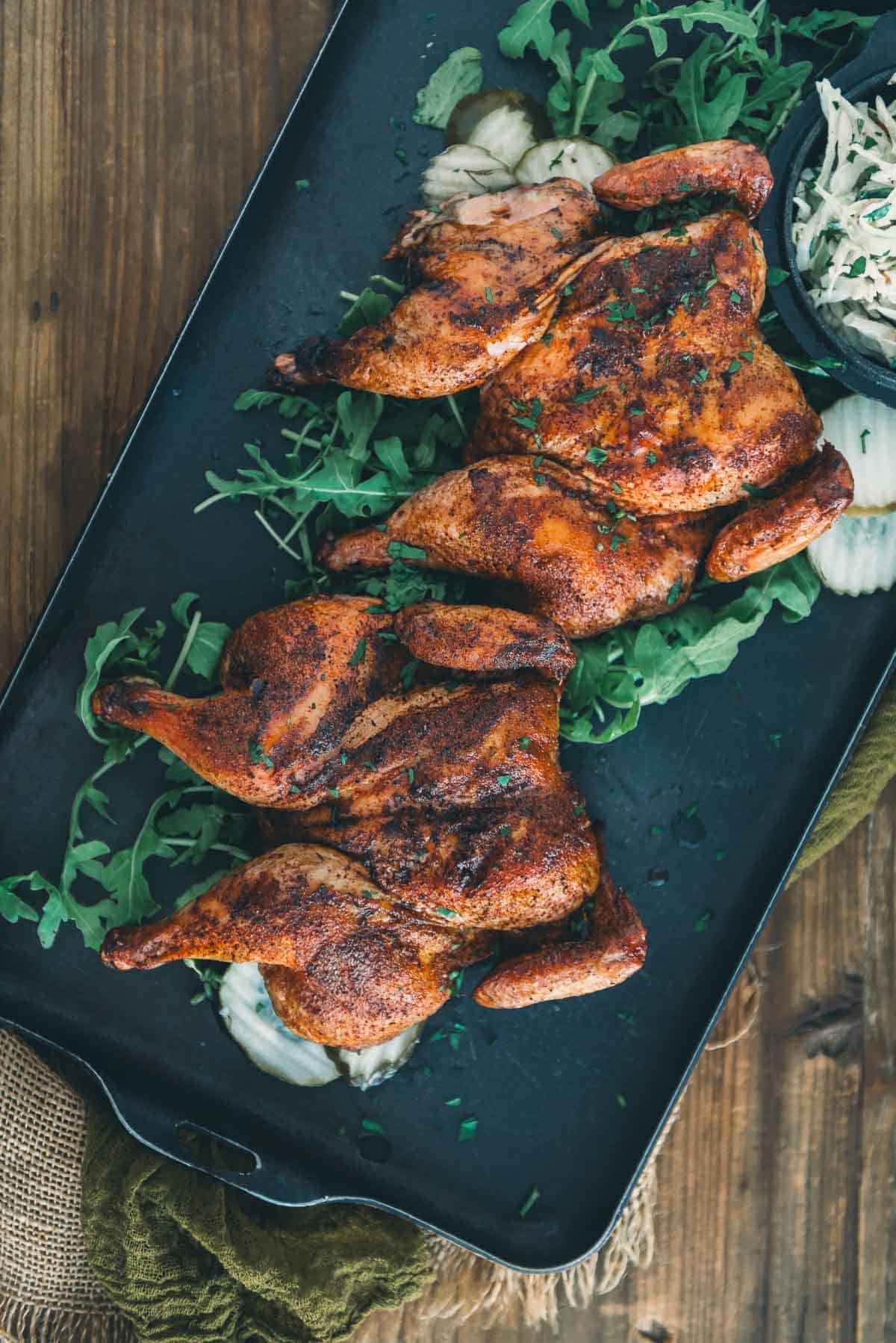 Smoked game hens on a black tray with greens.