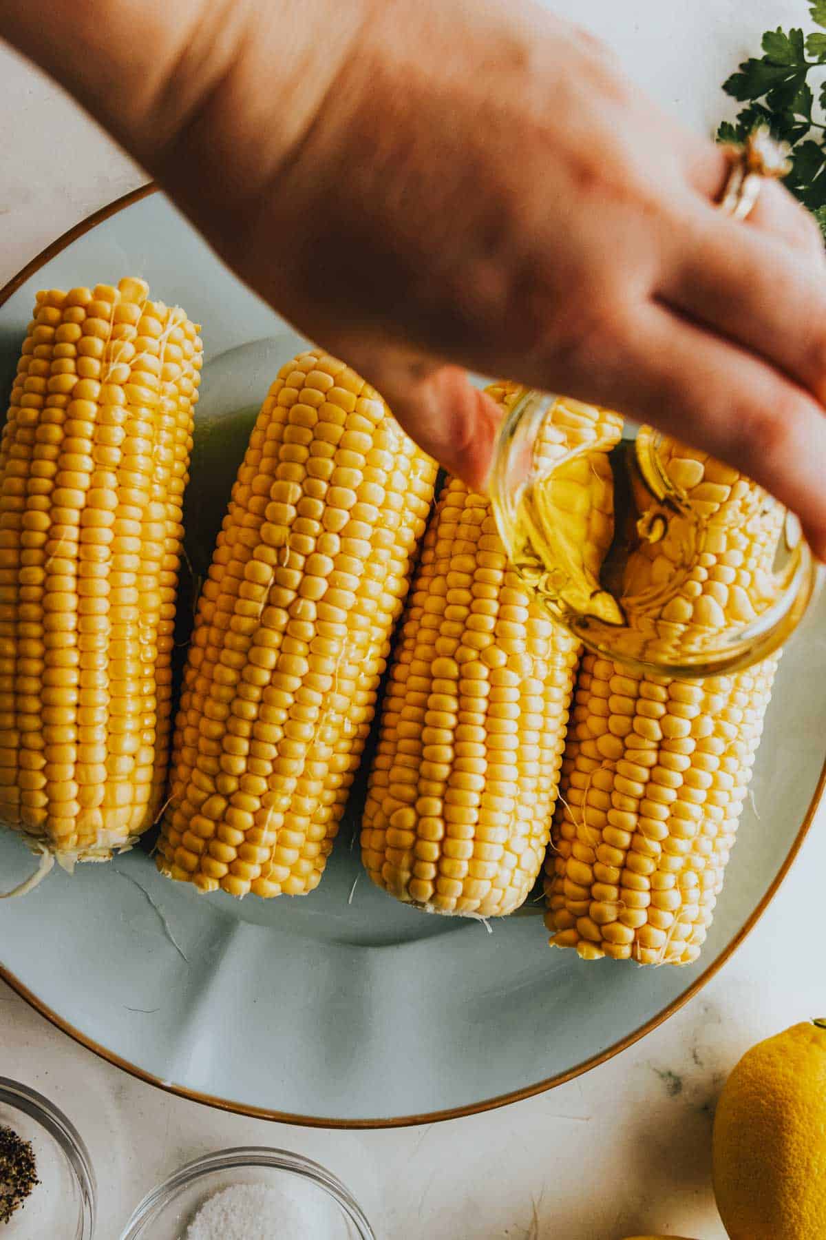 A person drizzling oil onto corn on the cob.
