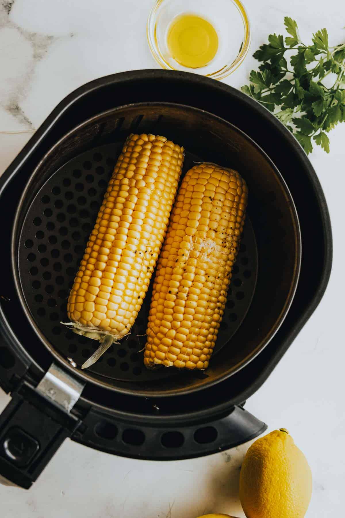 An air fryer with corn on the cob and lemons.
