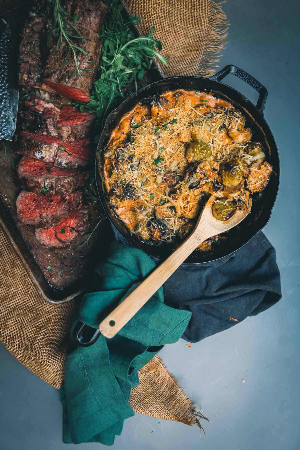 A skillet with brussels sprouts au gratin and a wooden spoon.