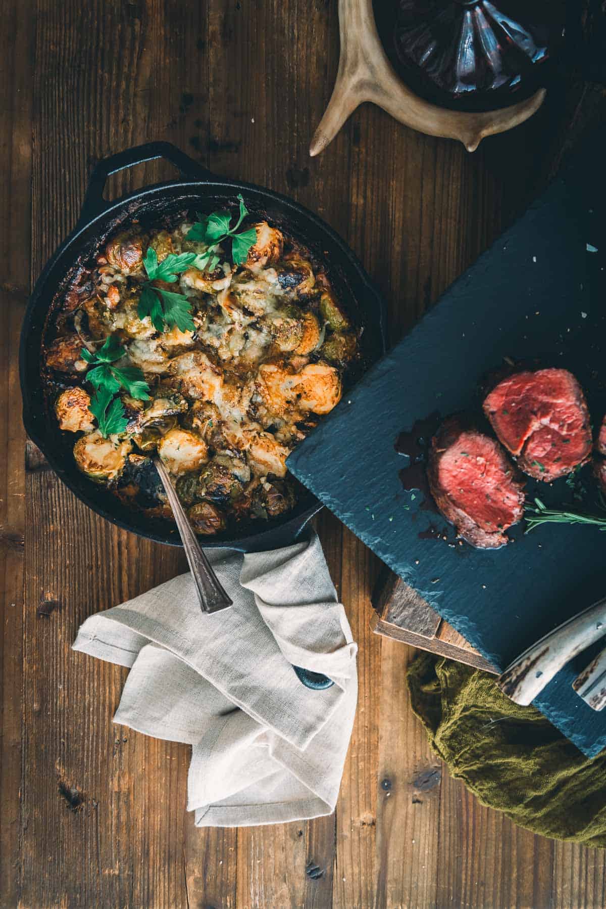 A skillet with cheesy brussels au gratin on a wooden table.