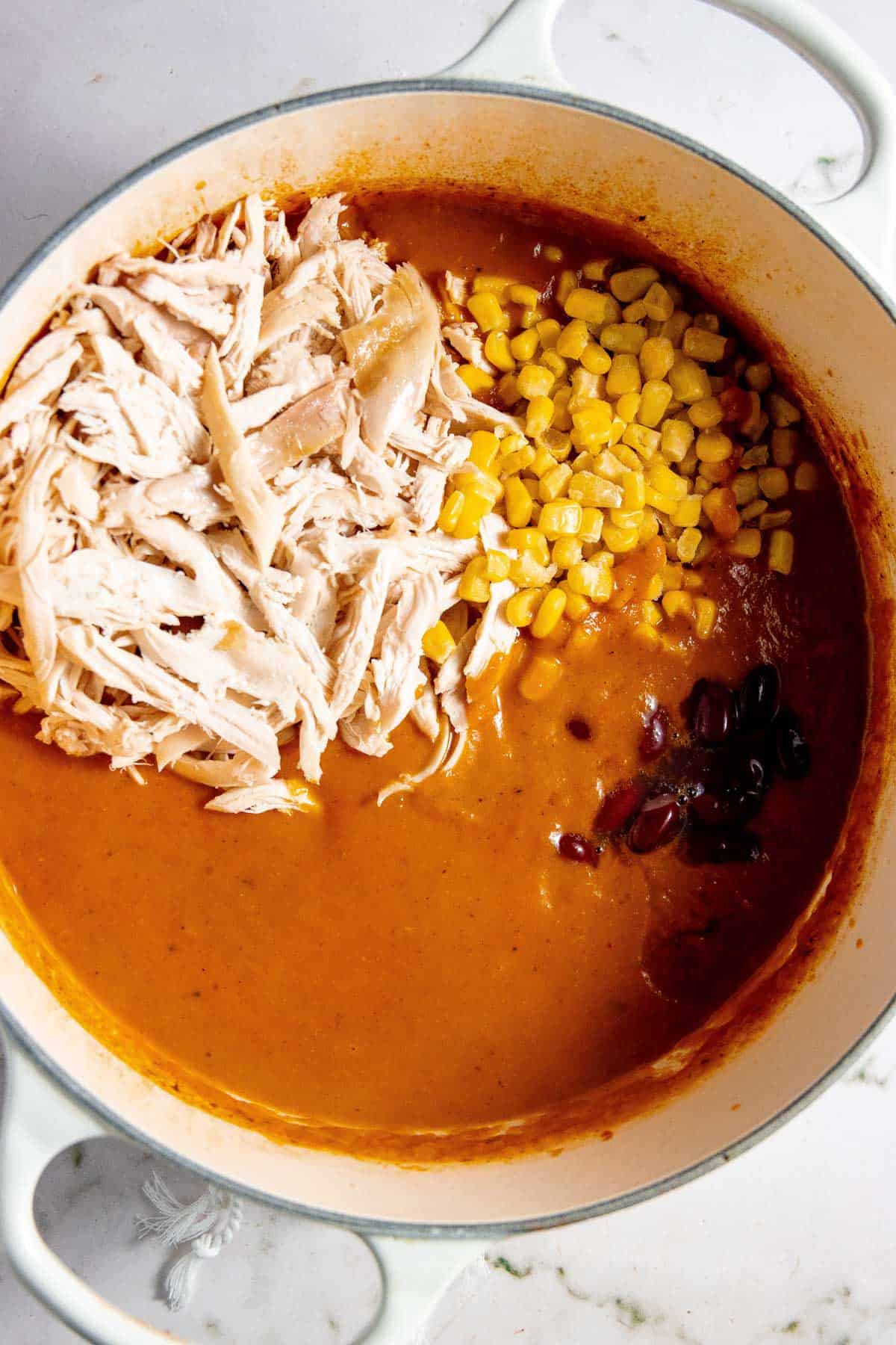 Enchilada chicken soup in a pot with corn and shredded chicken.