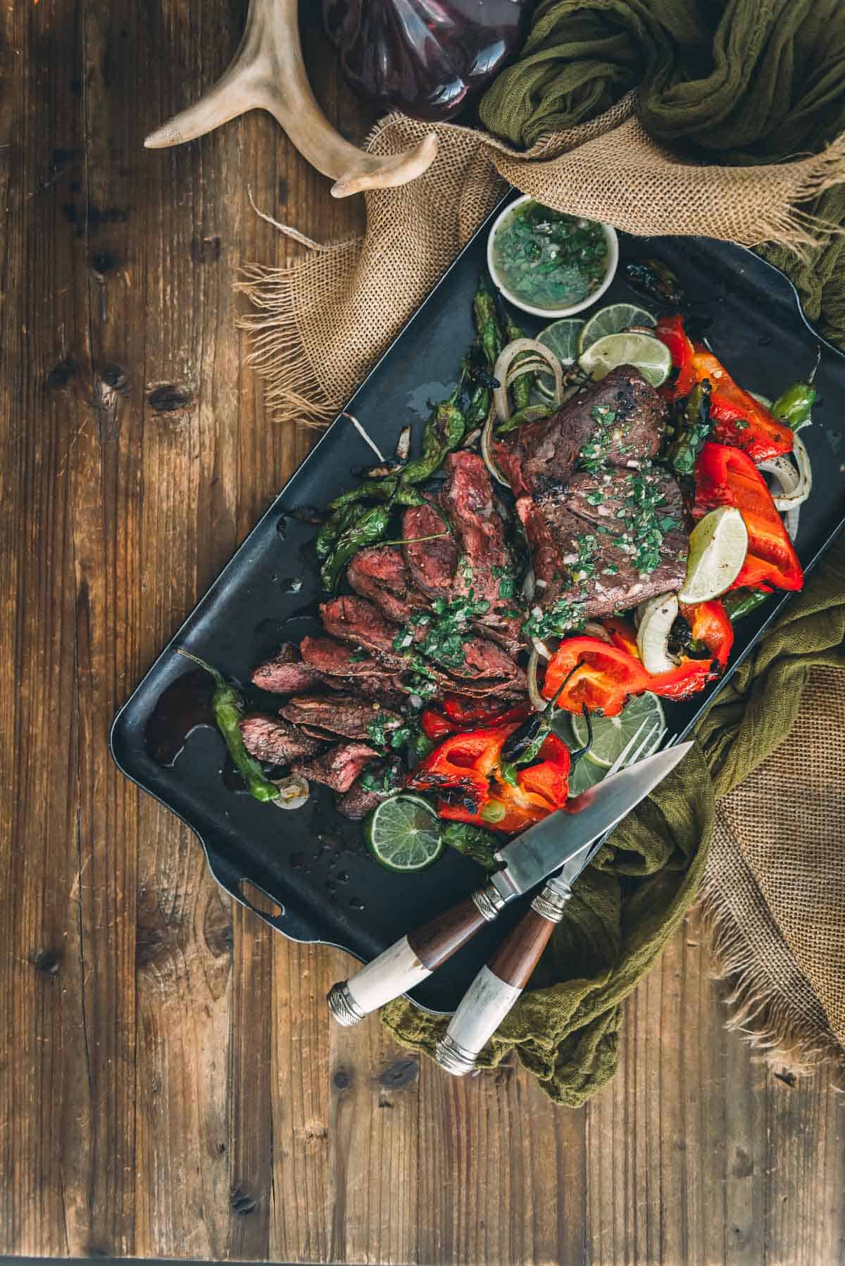 Grilled hanger steak on a black plate with peppers and herbs.