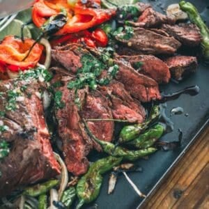 Grilled steak with peppers and onions on a black tray.