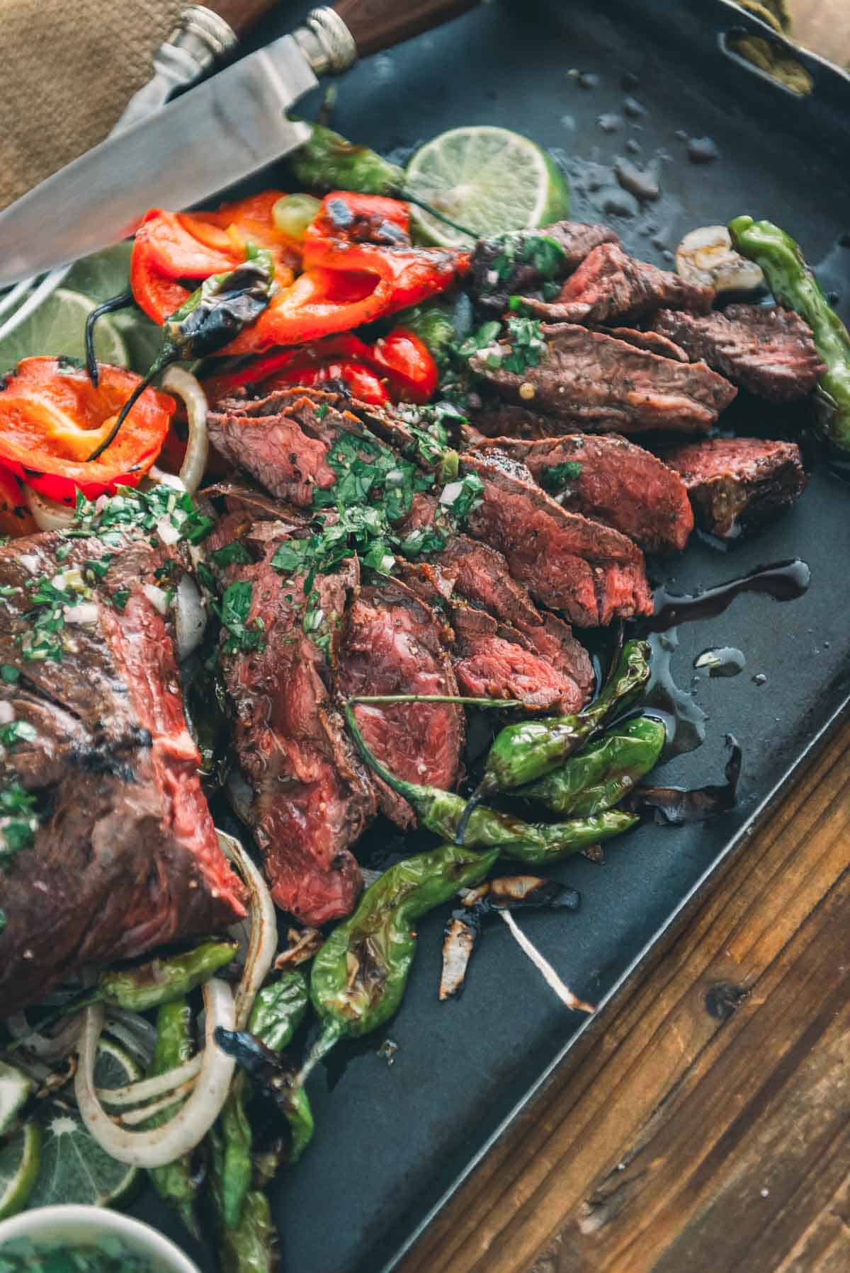 Grilled hanger steak with peppers and onions on a black tray.