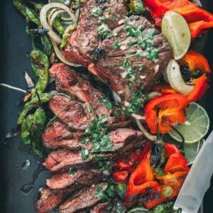 Grilled steak with peppers and lime on a black pan.