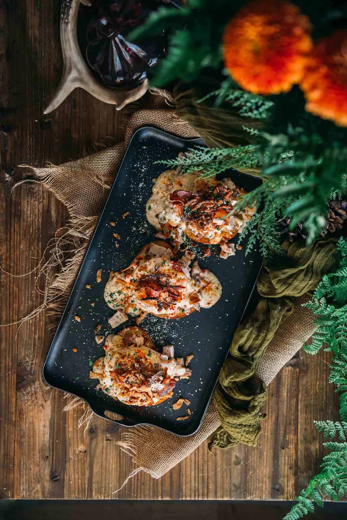 Hot brown sandwiches on a baking tray with herbs and spices on a wooden table.