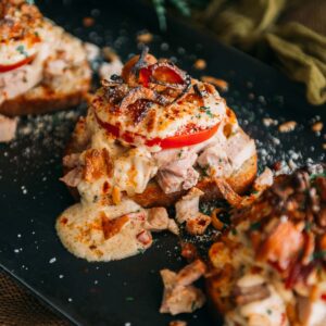 A black plate topped with toasted bread and turkey and melted cheese sauce.