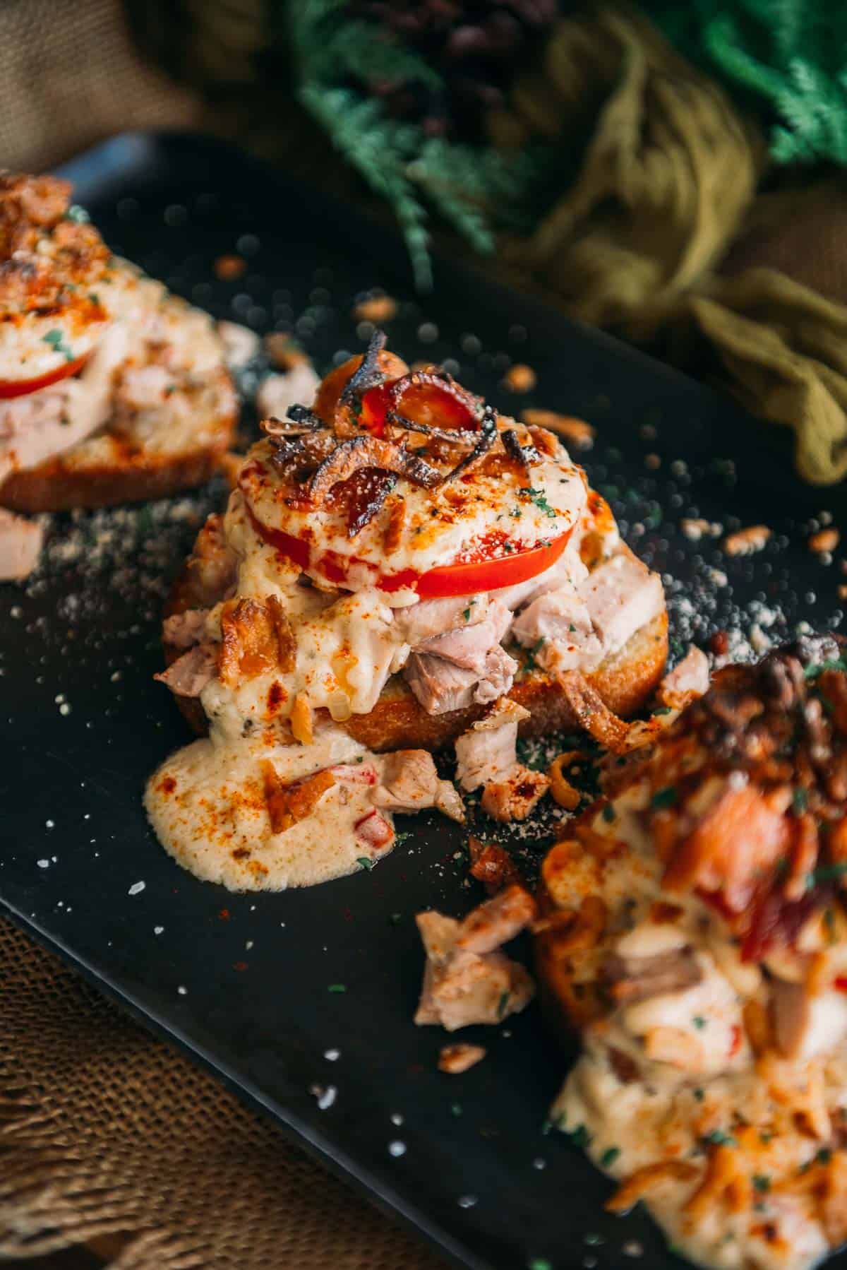 A black plate topped with toasted bread and turkey and melted cheese sauce.