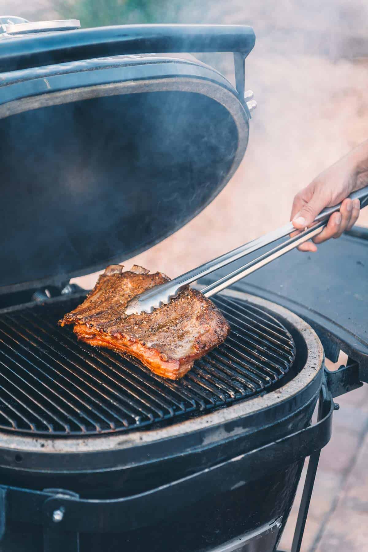 Ribs being placed fat side down on the grill with long tongs.