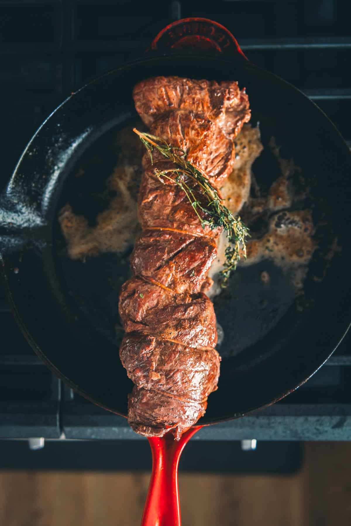 Beef tenderloin in a skillet with thyme and rosemary.
