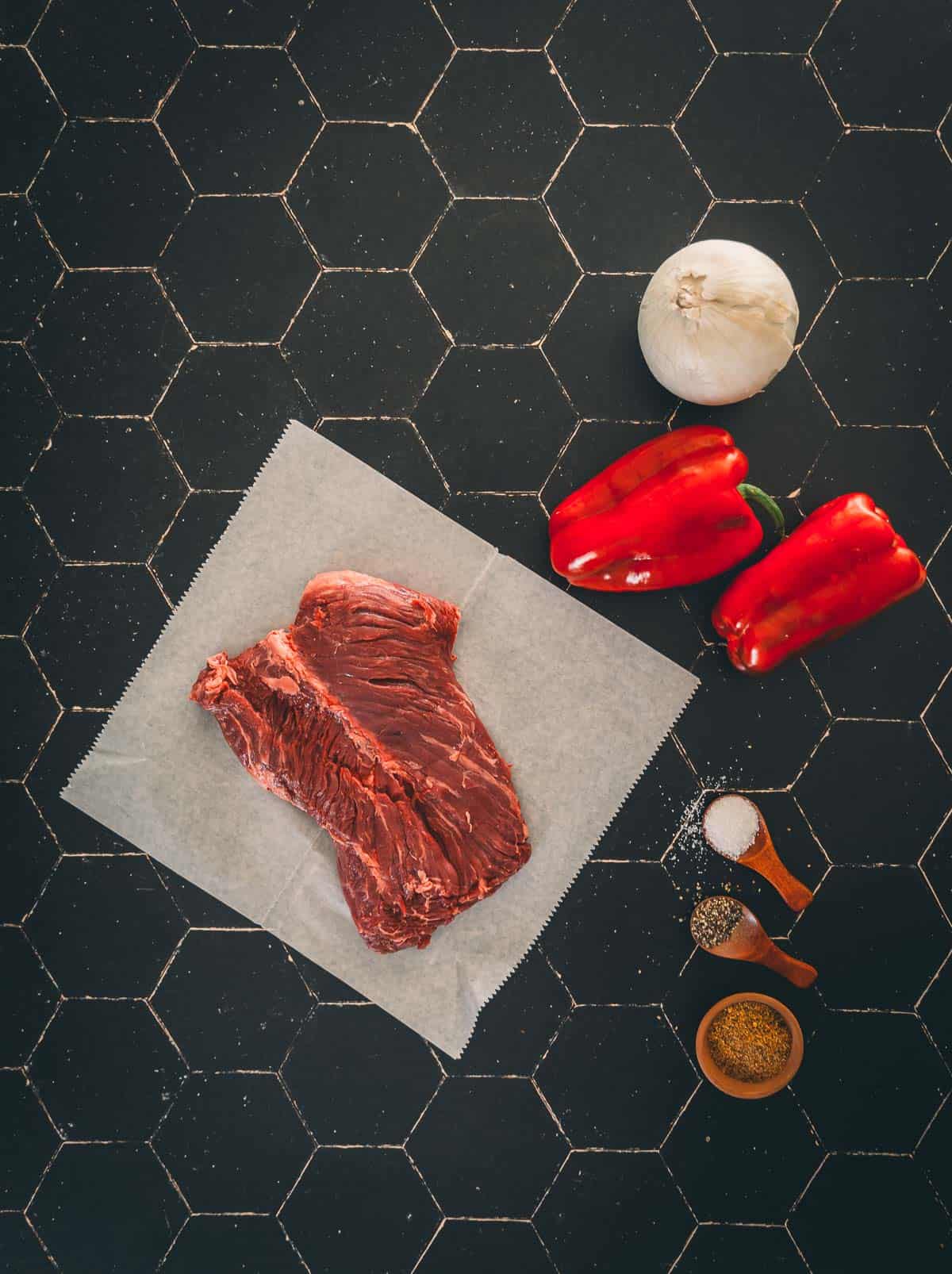 Ingredients for hanger steak with peppers and onions on a black background.