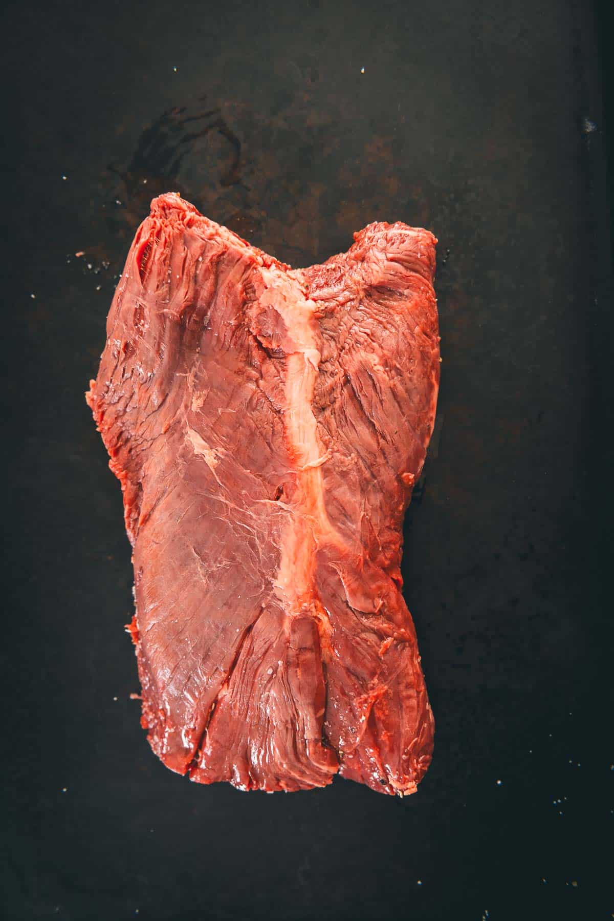 A piece of hanger steak on a black pan, showing signature connective tissue down the center.