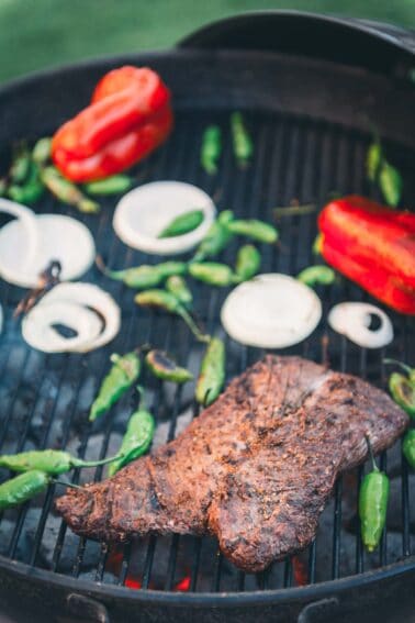 Hangers steak on a grill with peppers and onions.