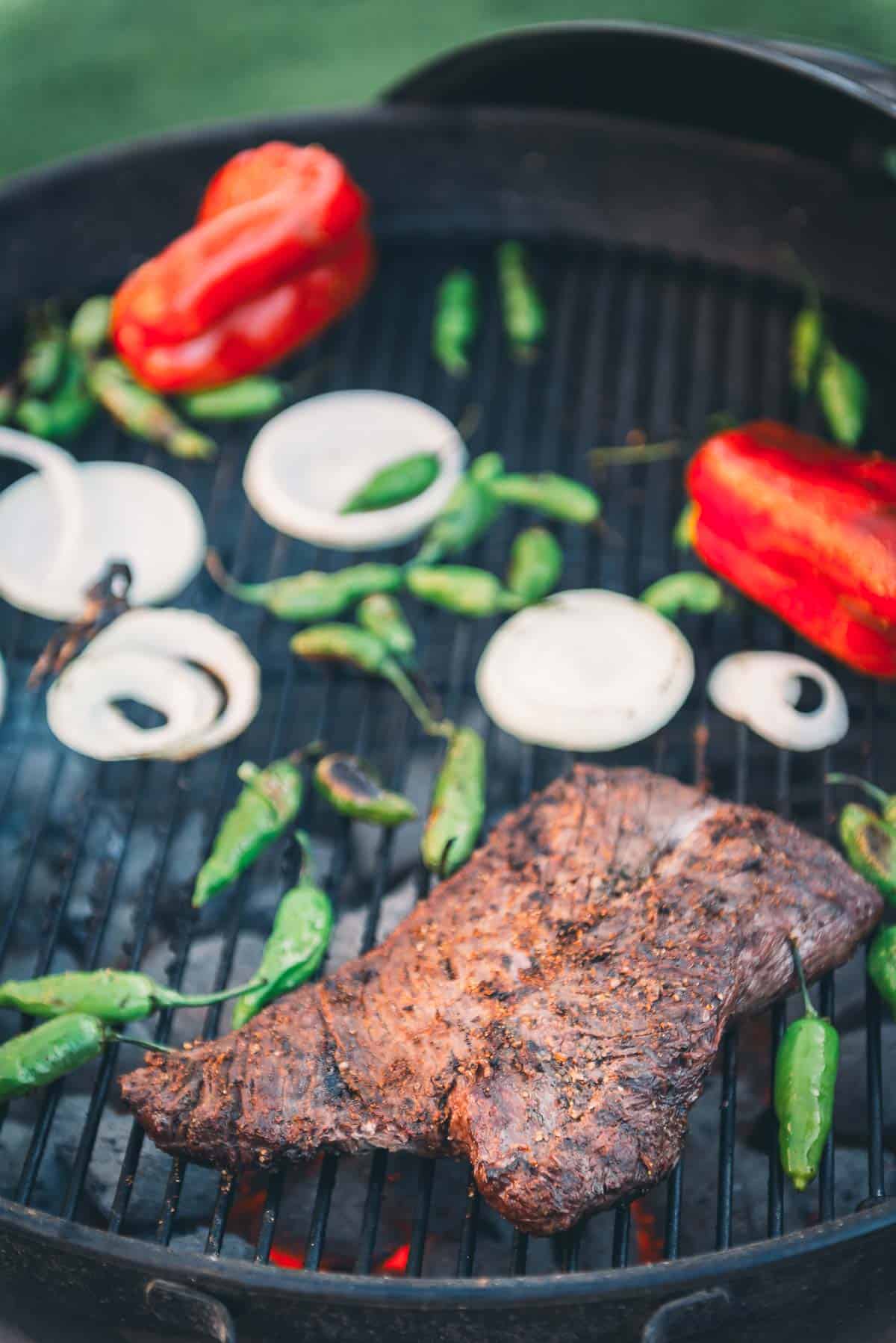 Hangers steak on a grill with peppers and onions.