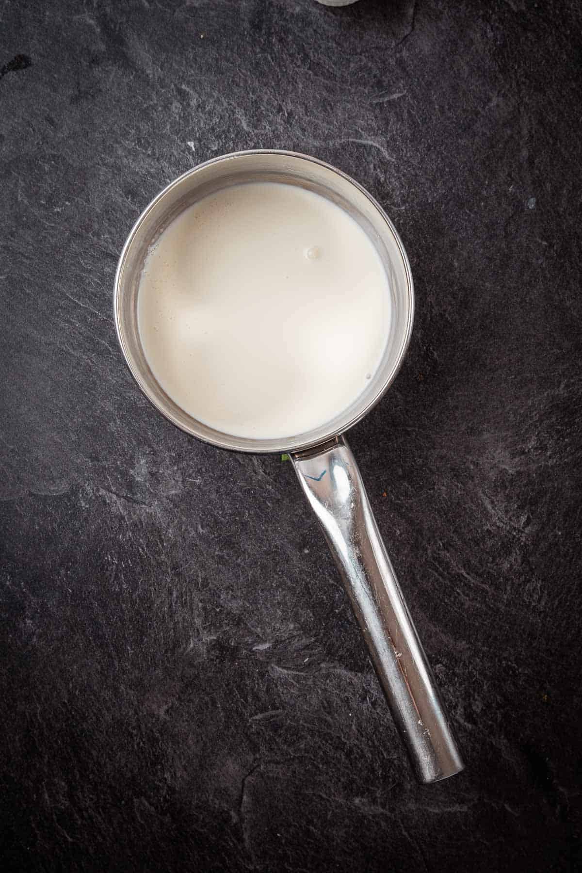 Milk in a metal pan on a dark surface.