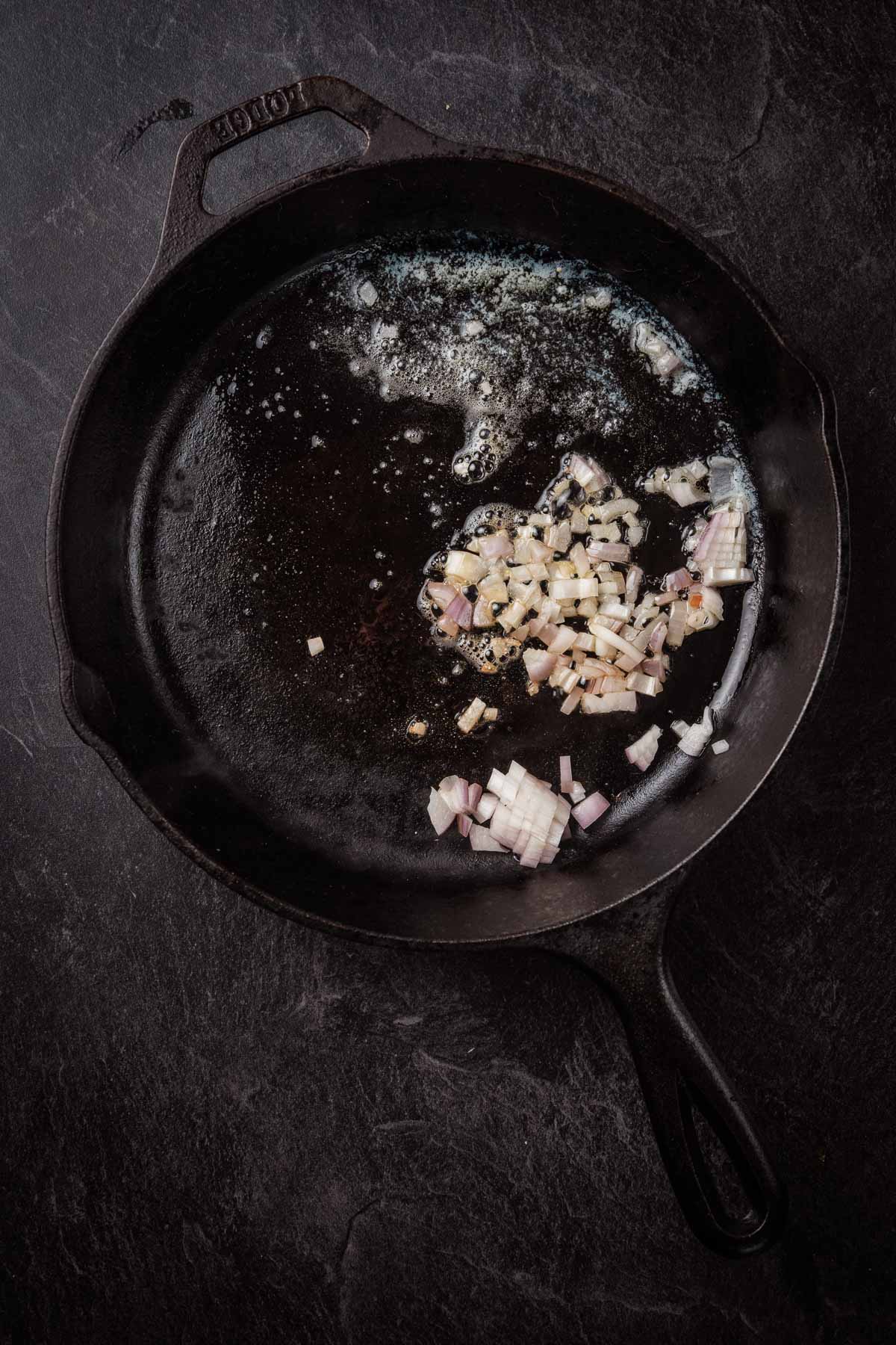 A frying pan with onions and garlic on a dark background.