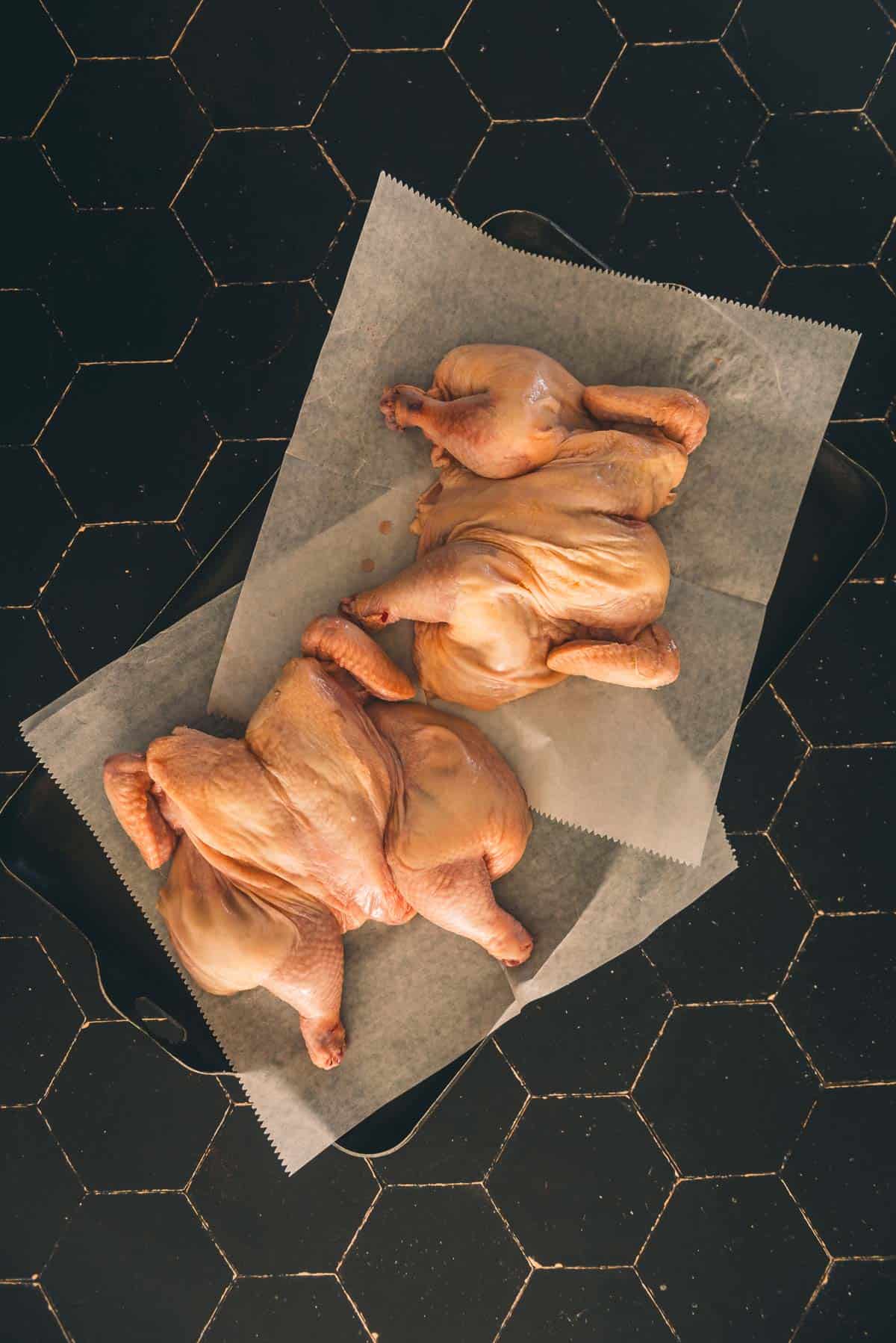 Two spatchcocked Cornish hens on a tray on a black background.