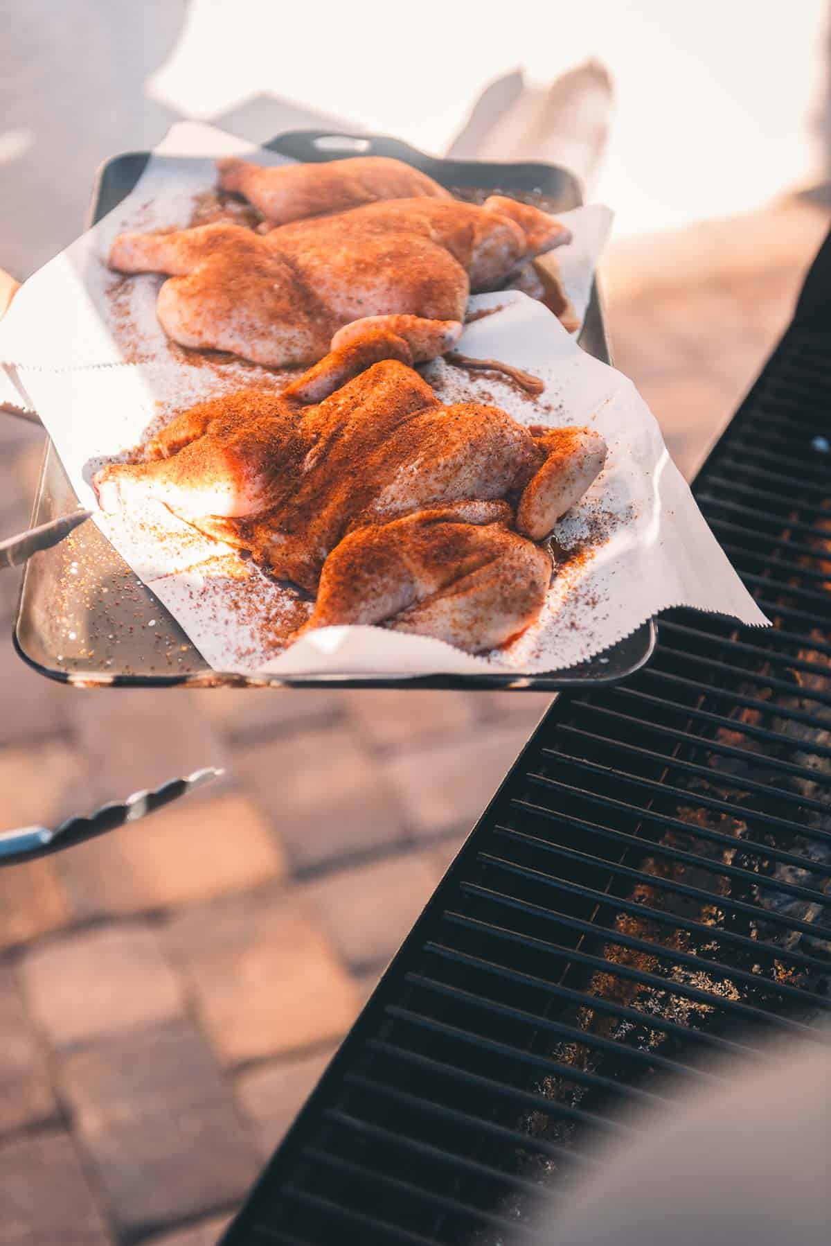 A person is holding a tray of game hens on a grill.
