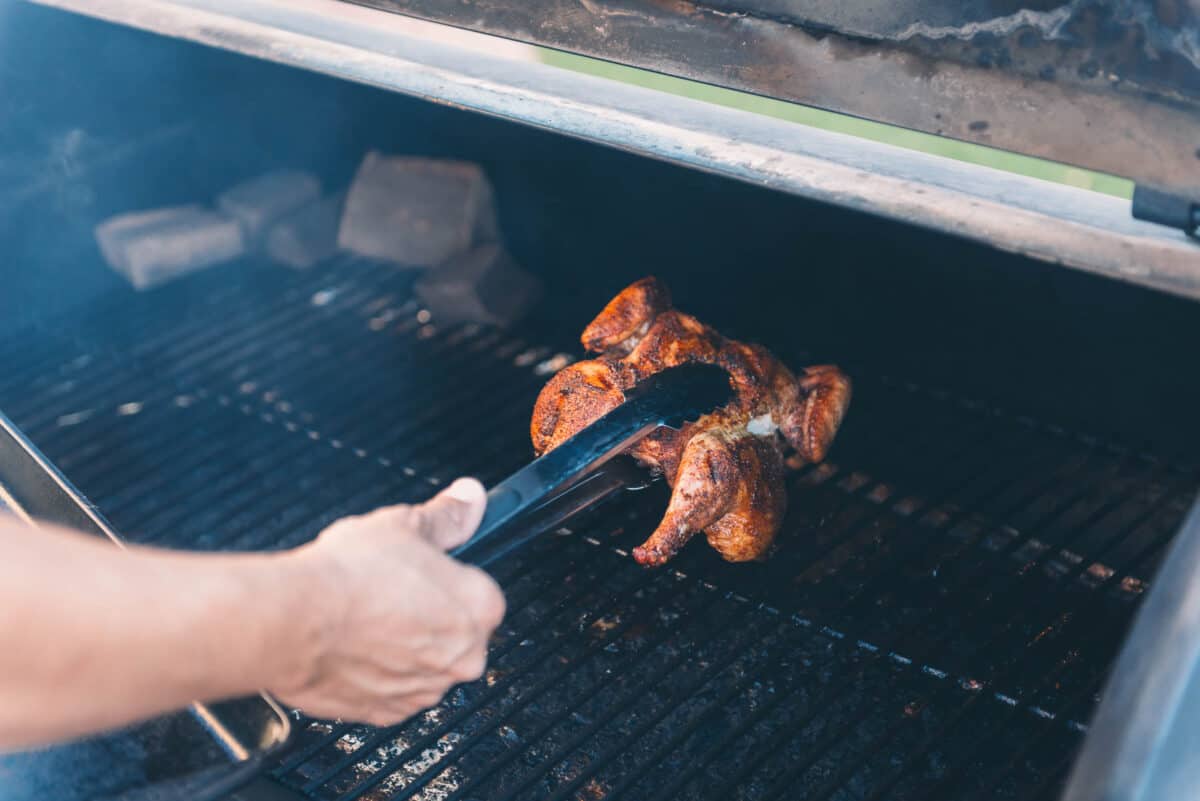 A person taking a game hen off the grill.