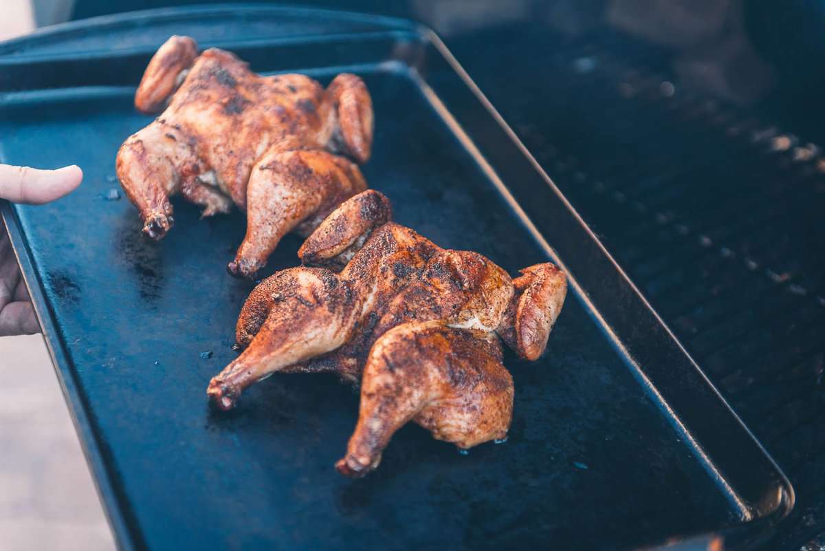 Two smoked cornish hens on a baking sheet coming off the grill.