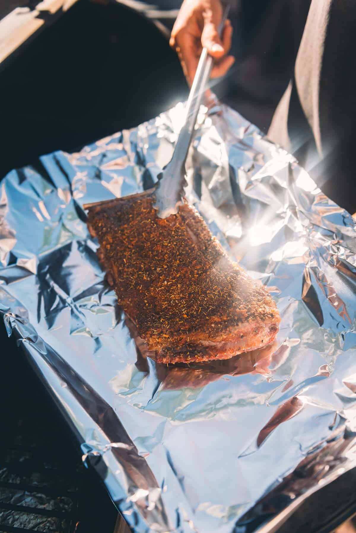 A person transferring a piece of meat on foil.
