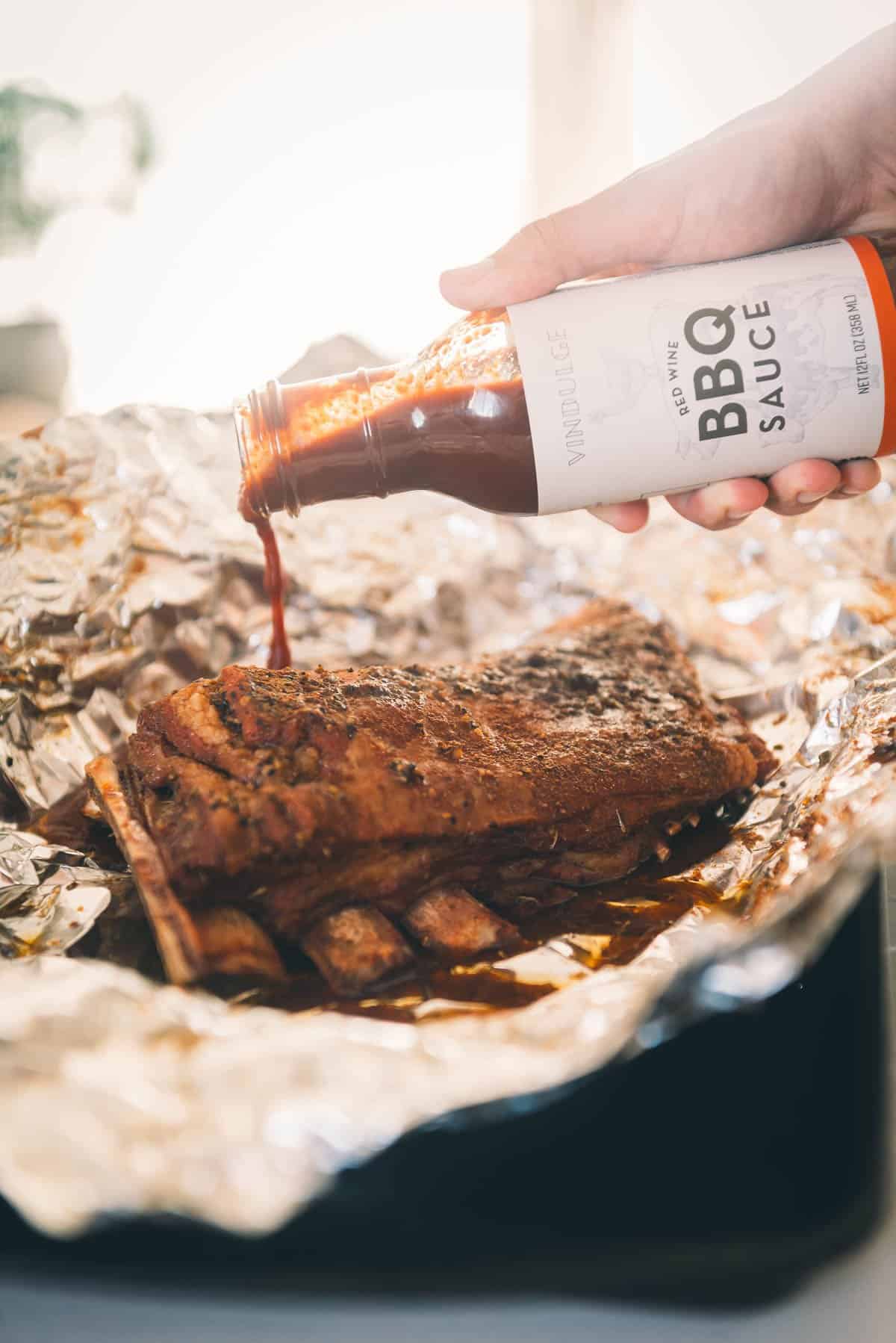 A person pouring bbq sauce onto a rack of ribs.