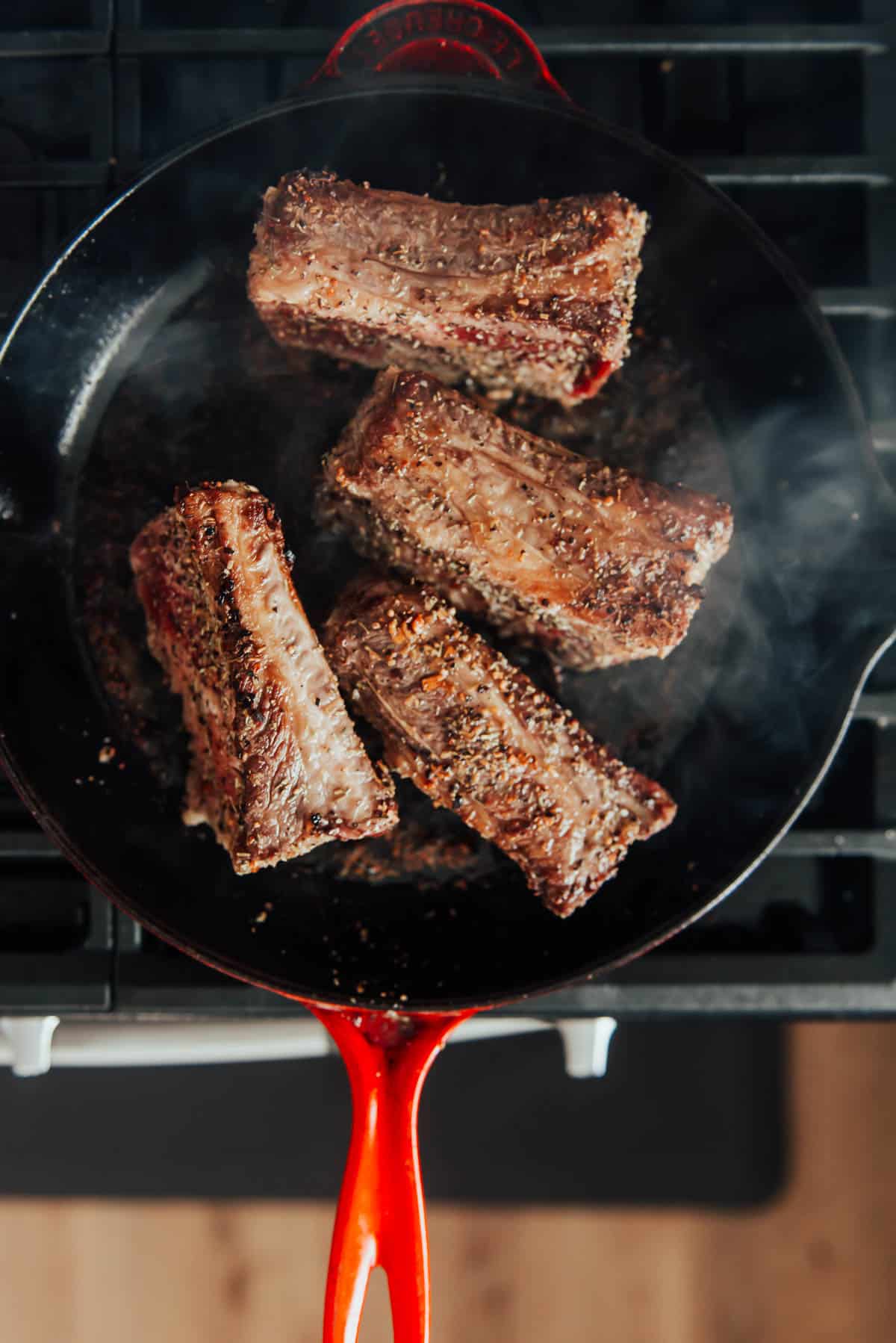 Beef ribs in a searing pan on a stove top.