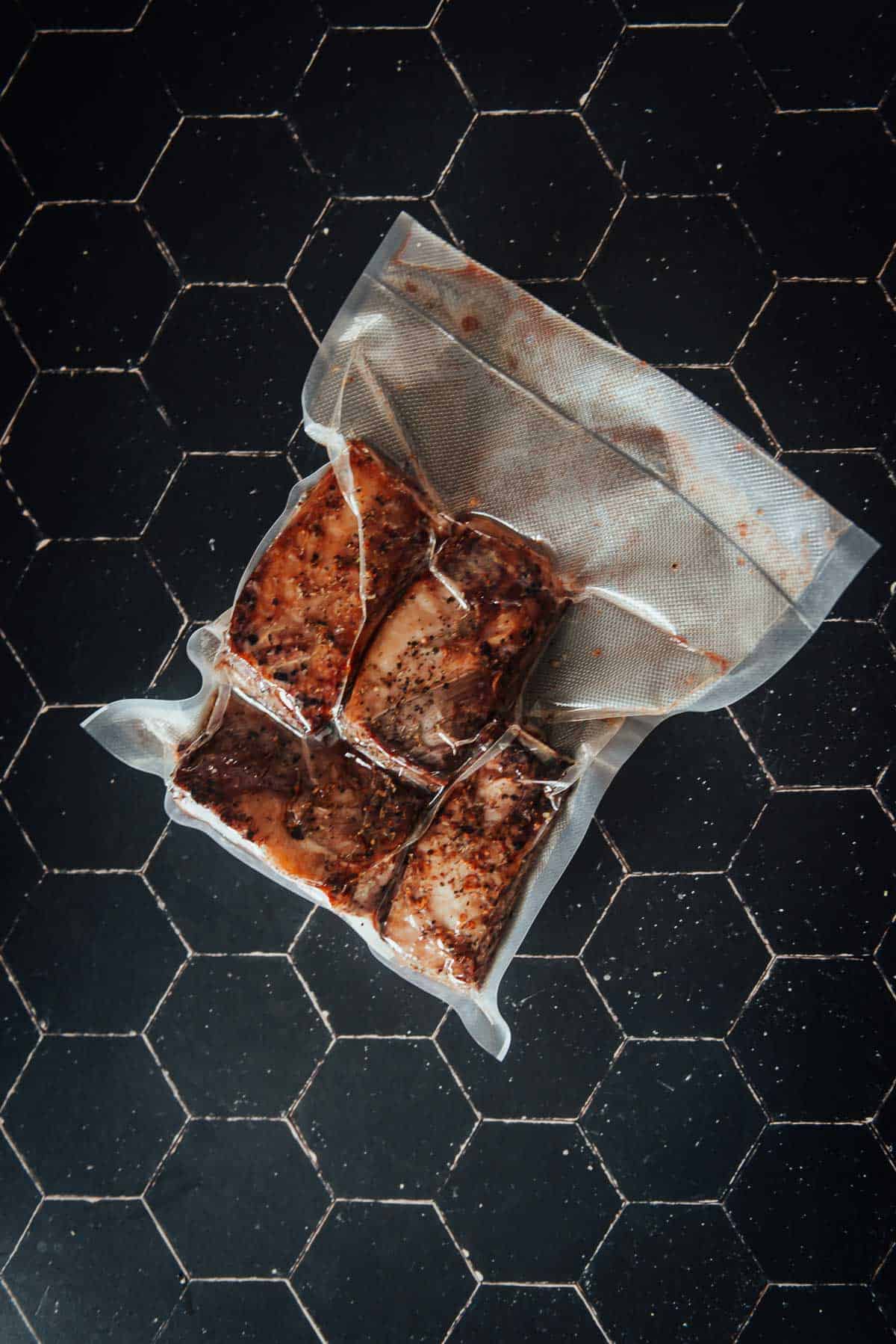 A short ribs in a plastic bag on a black surface.