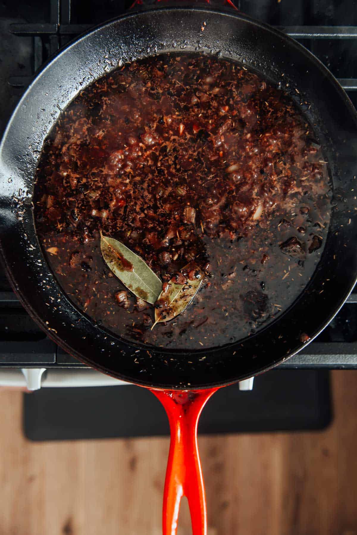 A cast iron pan on a stove with red wine sauce in it.