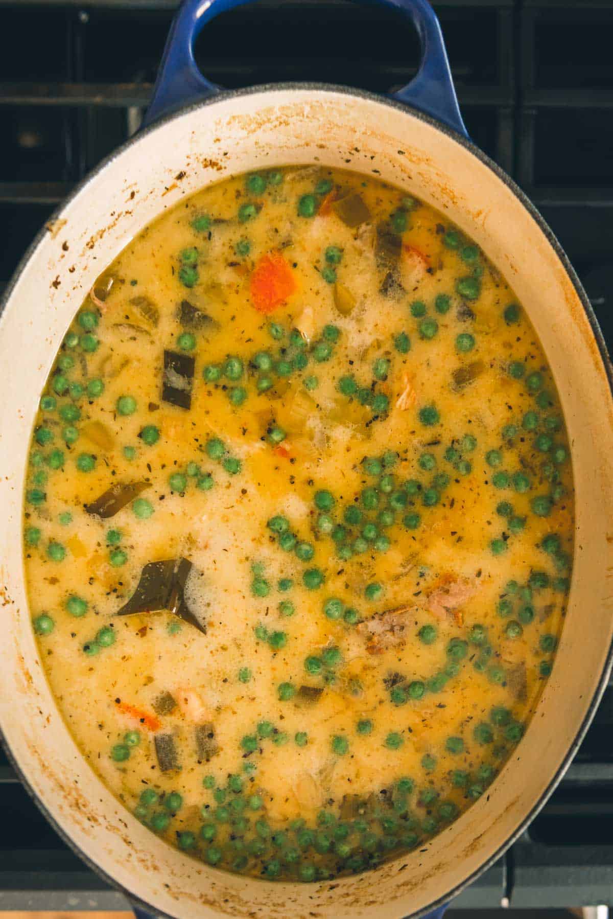 A pot of soup with peas and carrots on top of a stove.