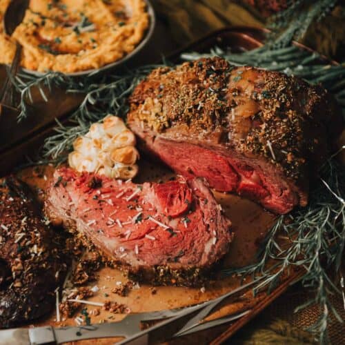 Standing rib roast on a wooden board with sprigs of rosemary.