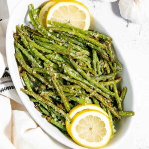 Green beans in a white bowl with lemon wedges.