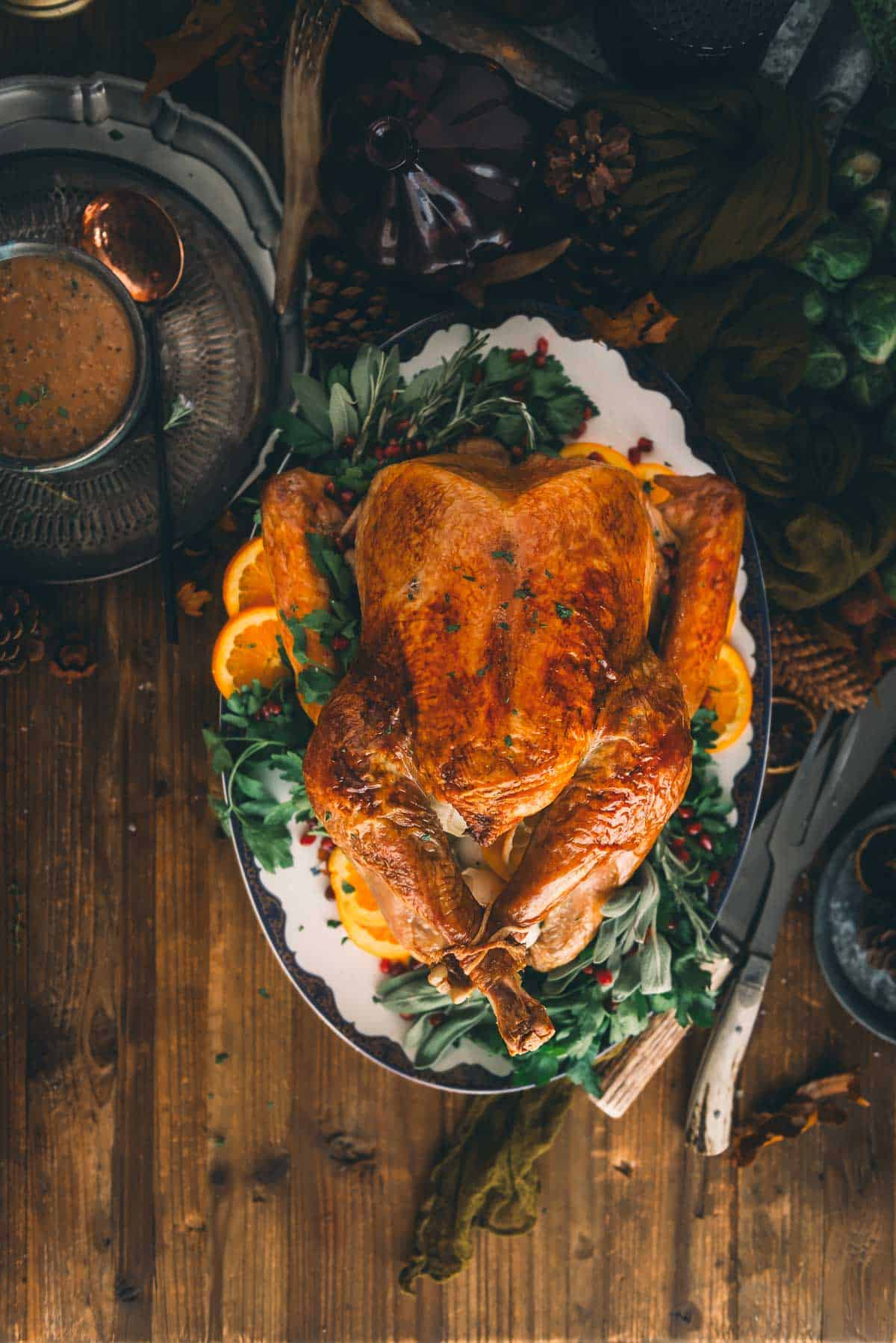 Roast turkey on a plater of herbs and sliced oranges.