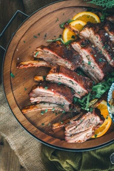 Smoked lamb ribs on a wooden platter with orange slices.