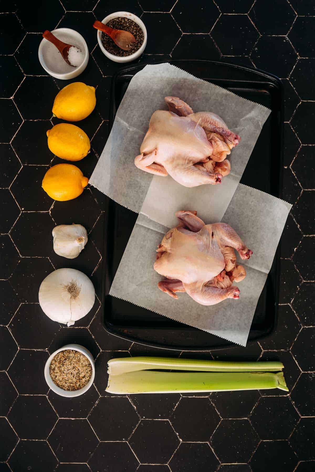 Ingredients including game hens, lemon and celery on a table for the recipe.