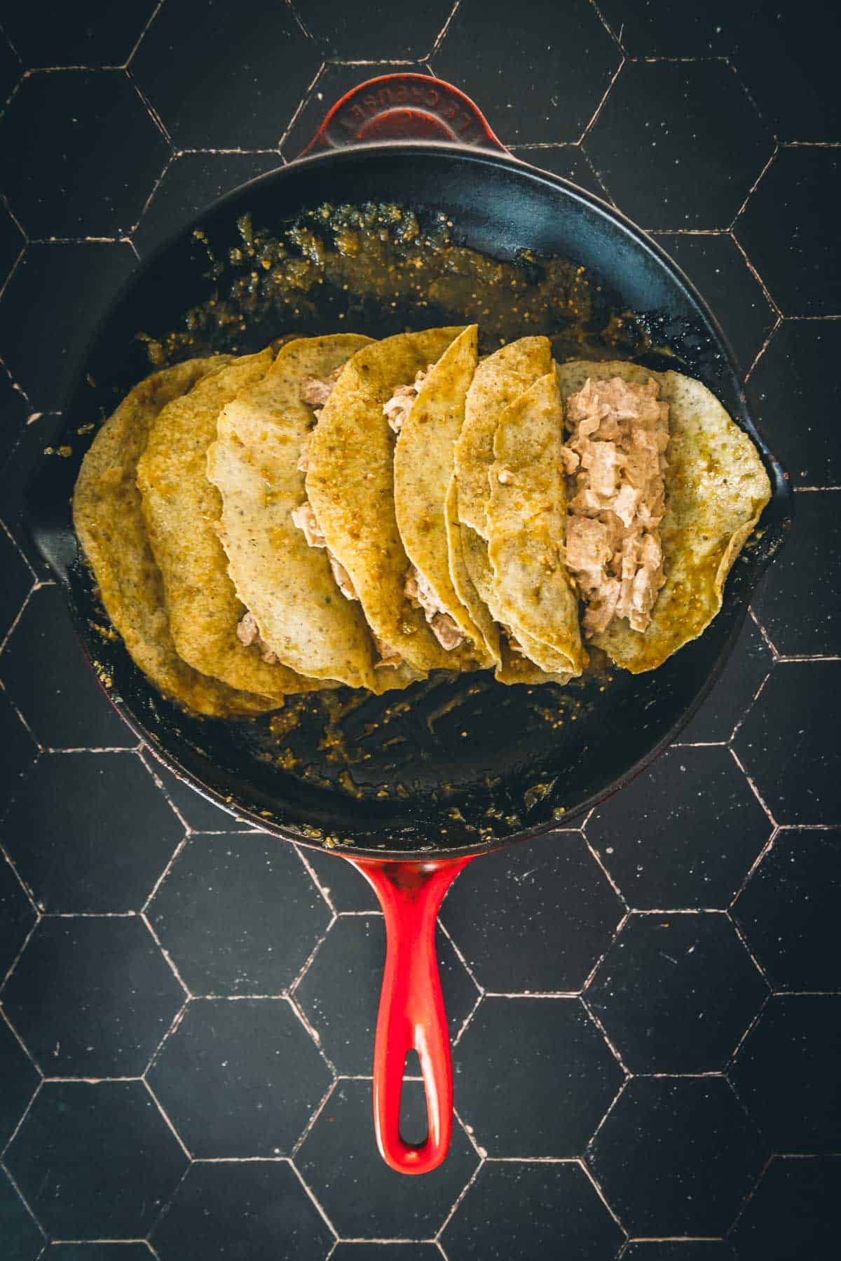 Tortillas in a frying pan on a black tiled floor.