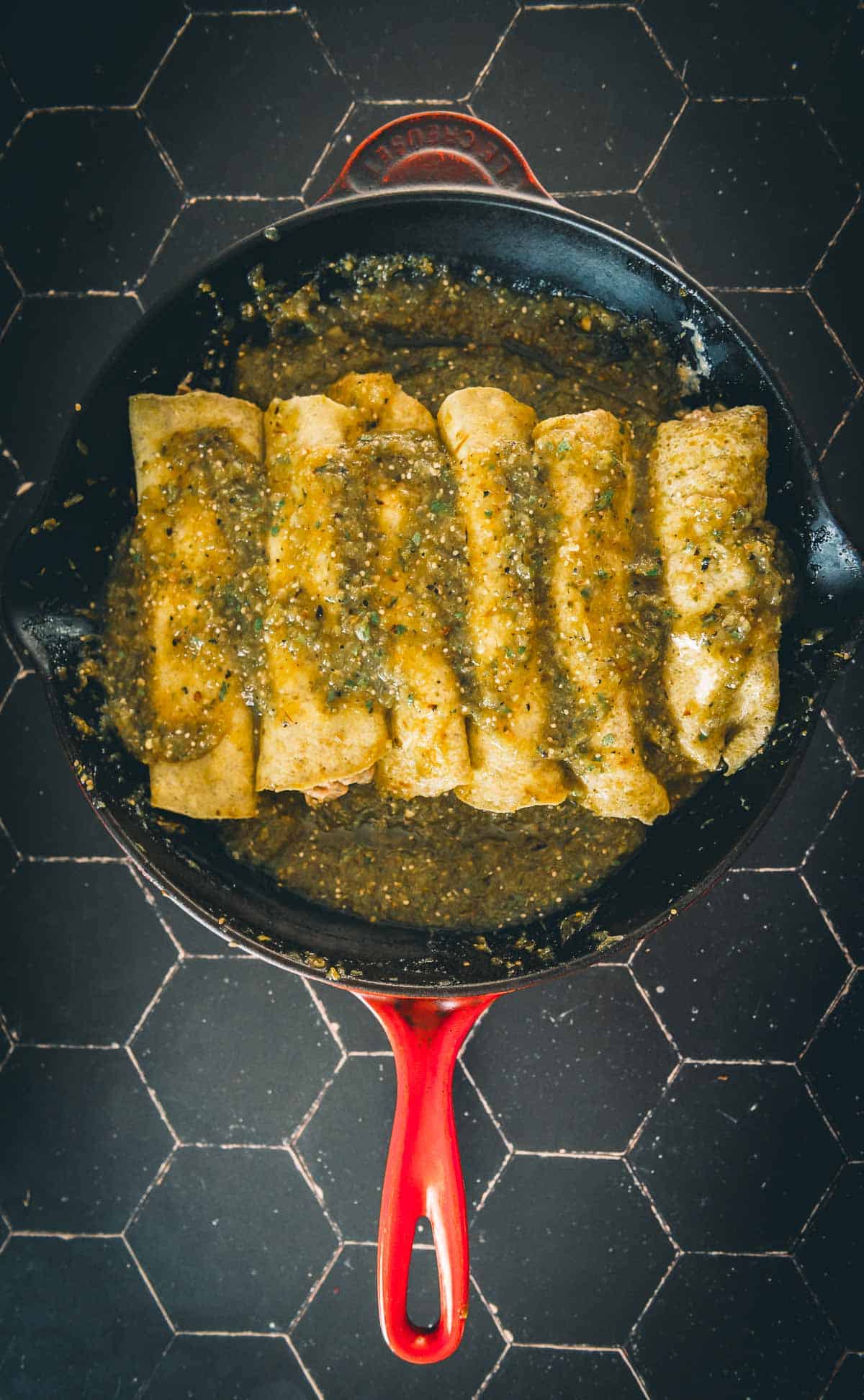 Enchiladas in a skillet with green sauce.