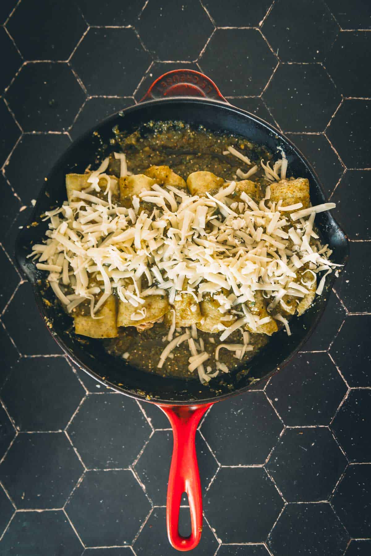 Cheese over top of the enchiladas in a red skillet.
