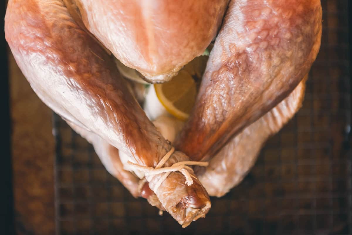 A turkey is sitting on a baking sheet, with legs tied together.